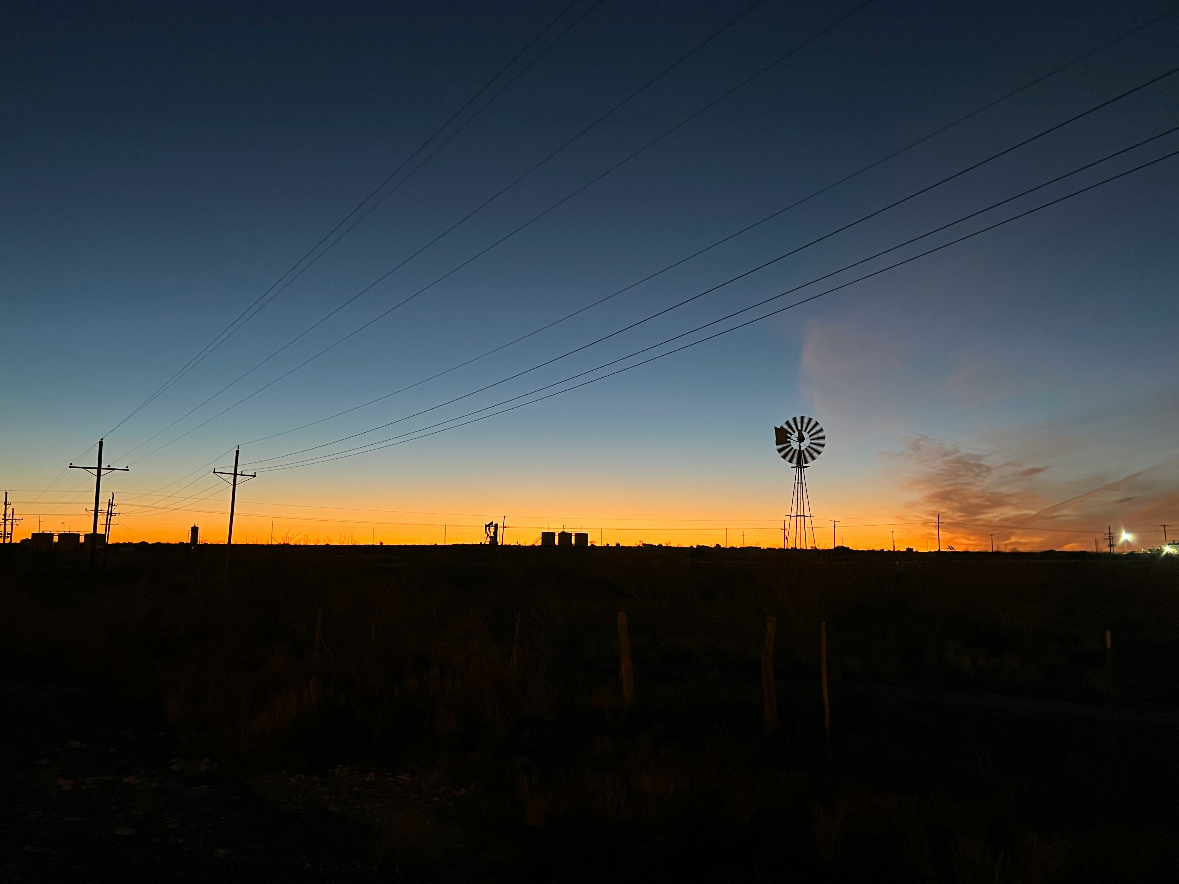 Oilfield silhouette at sunset — windmill and pumpjacks across the horizon